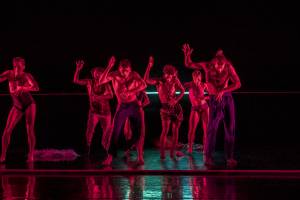 A group of dancers on stage under a red light